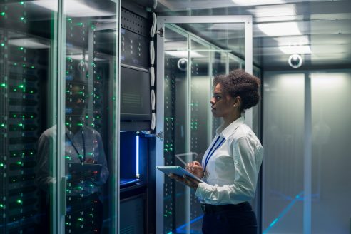 Female technician works on a tablet in a data center Medium shot of female technician working on a tablet in a data center full of rack servers running diagnostics and maintenance on the system